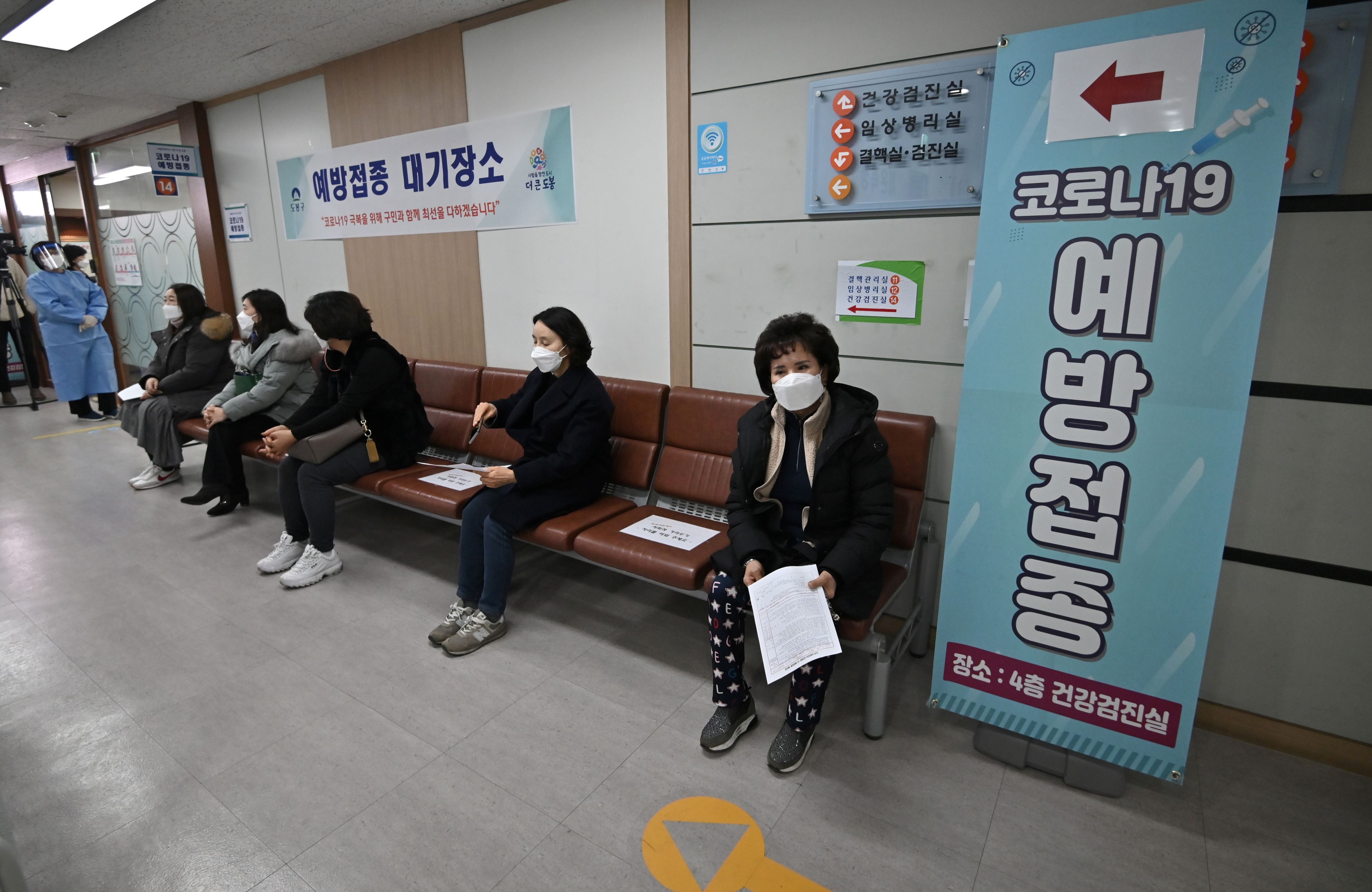 一群坐在商店前的人：韩国启动了COVID-19疫苗接种运动